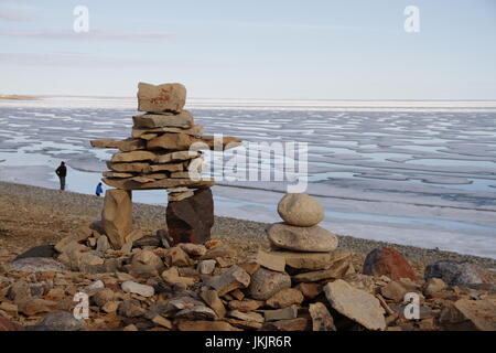 Inukshuk oder Inuksuk auf einem felsigen Strand mit Eis auf dem Ozean Ende Juni in der hohen Arktis in der Nähe der Gemeinde von Cambridge Bay Stockfoto