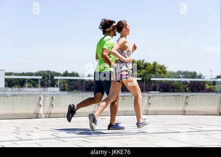 Schöner Mann und schöne Frau joggen zusammen auf der Straße zwischen den Wohnhäusern an einem sonnigen Tag Stockfoto