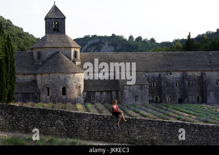 Frau sitzt an der Wand vor Lavendelfeld von Senanque Abbey, Gordes, Vaucluse, Provence-Alpes-Cote d ' Azur, Frankreich Stockfoto