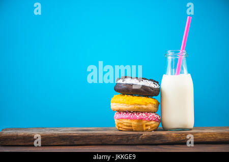 Milchflasche und Stapel von Donuts auf Holzbrett, Negativraum hellen Hintergrund Stockfoto