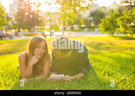 Sonnigen Porträt süßen jungen Paares liegen entspannen auf dem Rasen zusammen hört Musik im Kopfhörer auf Smartphone, Sommertag. Stockfoto