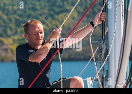 Junger Mann zieht die Seile auf die Segel des Schiffes. Segeln und Erholung. Stockfoto