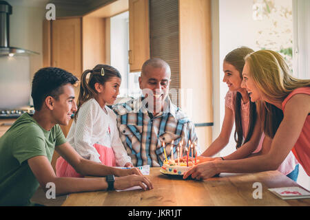 Glückliche Familie Väter Geburtstag mit einer Torte. Sie sind alle überfüllt Runde, als er bläst die Kerzen aus. Stockfoto
