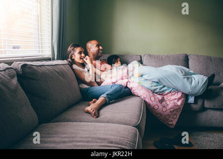 Vater zusammengerollt auf dem Sofa mit seinen beiden Töchtern. Sie befinden sich gerade einen Film mit Popcorn. Stockfoto
