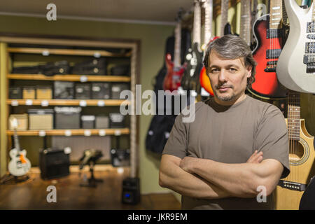 Porträt von zuversichtlich männlichen Besitzer stehen mit verschränkten von Gitarren im Shop Stockfoto