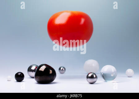 Tomaten in der Luft über kleine Runde Objekte unten vor grauem Hintergrund Stockfoto