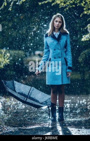 Volle Länge des Teenager-Mädchen mit Regenschirm stehen auf nassen Wanderweg im Regen Stockfoto