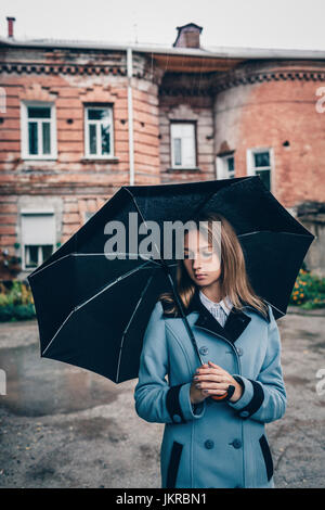 Nachdenklich Teenager-Mädchen hält Regenschirm stehen gegen Gebäude Stockfoto