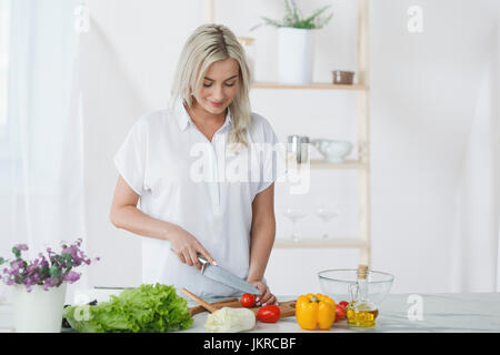 Lächelnde junge Frau hacken Tomaten auf Schneidebrett am Küchentisch Stockfoto