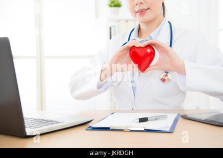 Nahaufnahme Foto ziemlich lächelnd Ärztin mit online-Service für Kardiologie Patienten und zeigen Herzmodell auf Schreibtisch. Stockfoto