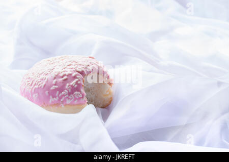 Rosa glasierten Donut mit einem Biss fehlt, Verlegung in weißen Laken Stockfoto