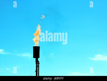 Ein Gas-Fackel-Stack wird vor einem blauen Himmel beleuchtet. Stockfoto