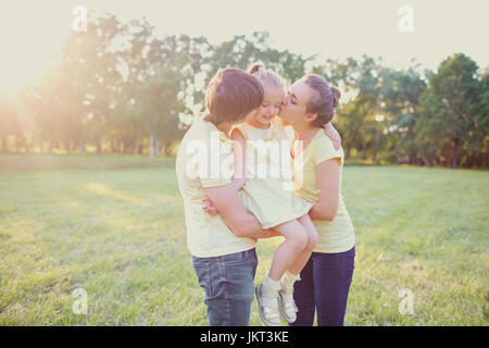 Arents küssen und umarmen ihre Tochter im Park. Stockfoto