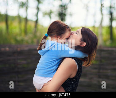 Glücklich liebende Familie. Mama hält ihre Tochter Kind Mädchen in die Arme und küßt sie auf die Stirn. Mutter und Tochter. Selektiven Fokus. Durchtrainierten Bild. Stockfoto