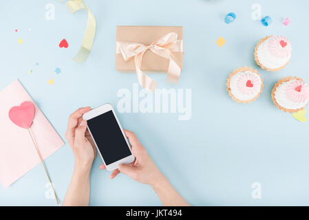 Draufsicht der menschlichen Hände halten Smartphone mit Kuchen und Geschenk-Box Mock-up, Geburtstagsparty Stockfoto