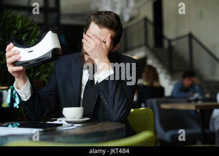 Müde Geschäftsmann hält Vr Kopfhörer beim Sitzen im café Stockfoto