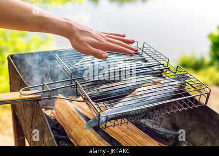 Gegrillter Fisch mit Gewürzen in Brand. Fisch grillen im Garten im Freien, an einem warmen sonnigen Tag. Stockfoto