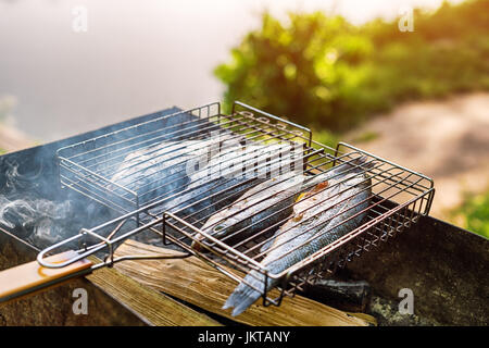 Gegrillter Fisch mit Gewürzen in Brand. Fisch grillen im Garten im Freien, an einem warmen sonnigen Tag. Stockfoto