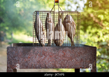 Gegrillter Fisch mit Gewürzen in Brand. Fisch grillen im Garten im Freien, an einem warmen sonnigen Tag. Stockfoto