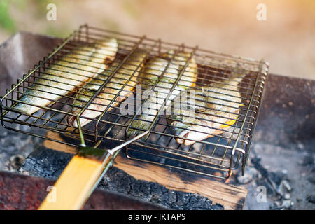 Gegrillter Fisch mit Gewürzen in Brand. Fisch grillen im Garten im Freien, an einem warmen sonnigen Tag. Stockfoto