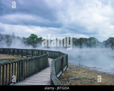 Holzbrücke reist durch geothermische Dampf bei Kuirau Park in Rotorua an einem bewölkten Tag mit dramatischen Wolken. Platz für Text. Stockfoto