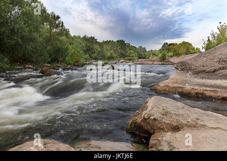 Der Fluss Südlicher Bug im Sommer - Felsküsten, Stromschnellen, schnellen Fluss, helle grüne Vegetation und ein bewölkter Himmel blau Stockfoto