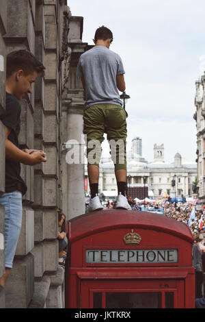 Der Zuschauer steht auf der roten Telefonzelle, während Fahnenträger während der Parade mit Weltflaggen marschieren. London 2017. Stockfoto