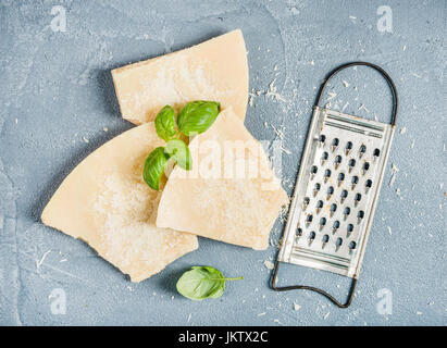 Kürzungen der Parmesan-Käse mit Metall Reibe und frischem Basilikum über konkrete strukturierten Hintergrund Stockfoto