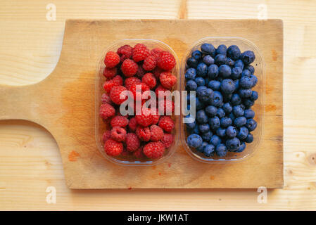 Heidelbeeren und Himbeeren in Kunststoff-Container-Boxen auf Holztisch Stockfoto