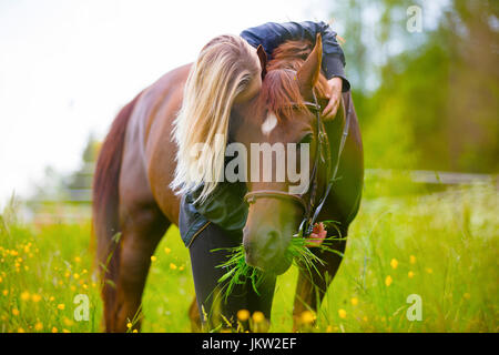 Blonde Frau auf einer Wiese umarmt ihr Arabisches Pferd Stockfoto