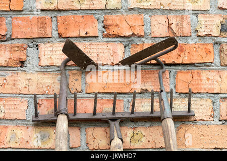 Stillleben mit alt / rostig, Rechen und Hacke Gartenwerkzeuge im Hintergrund alte verwitterte Ziegel machen horizontale Linien. Stockfoto