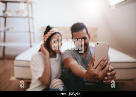 Aufnahme des jungen Paares zu Hause sitzen und nehmen Selfie mit Handy. Smartphone in Händen eines Mannes im Vordergrund. Stockfoto