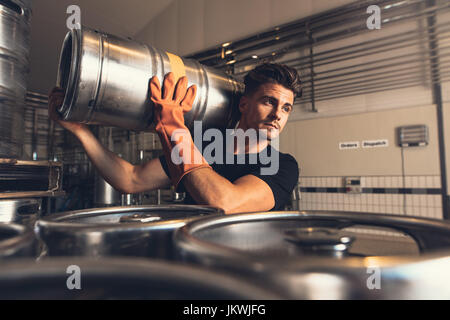 Schuss von Brewer Keg werkseitig Brauerei tragen. Junger Mann mit Metall Bierfässer auf Lager. Stockfoto