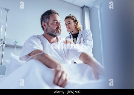 Hospitalisierten Mann immer von weiblichen Arzt untersucht. Arzt überprüfen Herzschlag männlichen Patienten im Krankenzimmer. Stockfoto