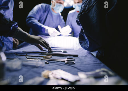 Nahaufnahme der Krankenschwester unter medizinische Instrumente für den Betrieb mit Kollegen tun Chirurgie im Hintergrund. Medizinisches Team die Operation im Krankenhaus. Stockfoto