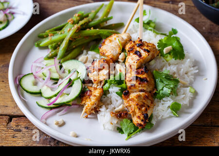 Satay-Hähnchen-Spieße mit grünen Bohnen, Reis und Gurkensalat Stockfoto