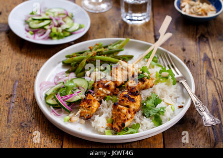 Satay-Hähnchen-Spieße mit grünen Bohnen, Reis und Gurkensalat Stockfoto