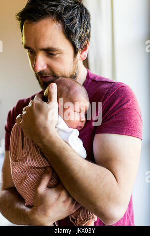 Junger Vater zu Hause hält sein neugeborenes Mädchen. Stockfoto