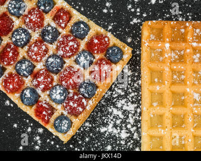 Himbeeren und Heidelbeeren auf geröstetem Waffel vor schwarzem Hintergrund Stockfoto