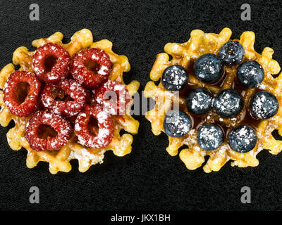 Zwei belgische Butter-Waffeln garniert mit frischen Himbeeren und Heidelbeeren gegen ein schwarzer Hintergrund Stockfoto