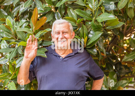 Porträt des Lächelns salutieren Fett älterer Menschen auf dem Hintergrund der Blätter der Magnolie Stockfoto