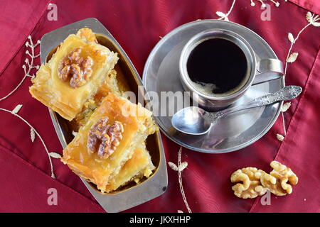 Traditionelle griechische Baklava mit Filo-Teig, Zuckersirup und Wallnuts auf einem Metalltablett mit Metall Kaffeetasse auf lila Tuch Hintergrund gemacht. Stockfoto