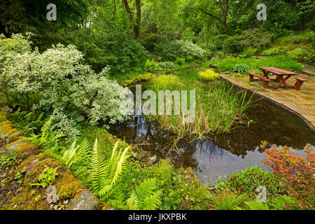 Spektakuläre Gemeinschafts-Garten mit Wasserspiel, Pflasterarbeiten, Picknick-Tisch und Bäume spiegeln sich im Wasser des ruhigen Pool - in Schottland Stockfoto