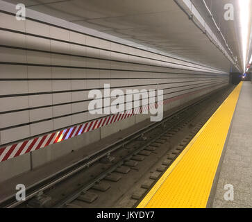 Blick auf die Bahngleise vom Bahnsteig in einer New York City U-Bahnstation. Weiße U-Bahnfliesen und eine gelbe Linie auf der Plattform in NY. Stockfoto