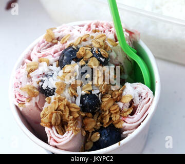 Rühren Sie Gebratenes Eis Brötchen gemacht mit Erdbeereis, garniert mit Heidelbeeren, Müsli und Kokosnuss in einer Schüssel Stockfoto