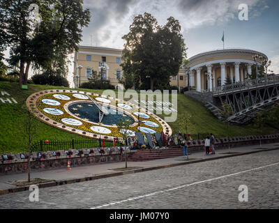 KIEW, UKRAINE - 10. JUNI 2016: Blumenuhr auf der Heroyiv Nebesnoyi Sotni Allee mit internationalem Zentrum für Kultur und Kunst (Oktoberpalast) in Backgro Stockfoto