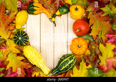 Bunte herbstliche Laub und Kürbisse liegen in Herzform auf Holzbrettern Stockfoto