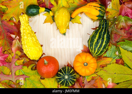 Bunte herbstliche Laub und Kürbisse liegen in Herzform auf Holzbrettern Stockfoto