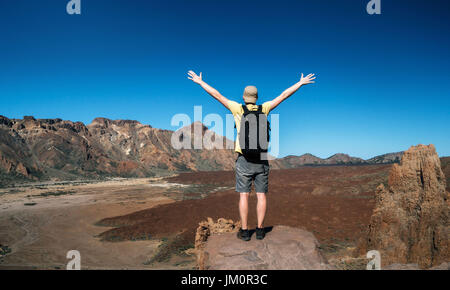 Mann mit einem Rucksack steht Rücken zur Kamera mit erhobenen Händen. Reisende genießen die Landschaft mit Bergtal im Krater des Teide Kra Stockfoto