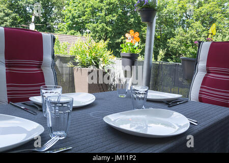 Überdachter Balkon mit Tisch mit weißen Platten, Trinkgläser und Esstisch mit zwei Stühlen mit modernen Sitzbezüge. Stockfoto